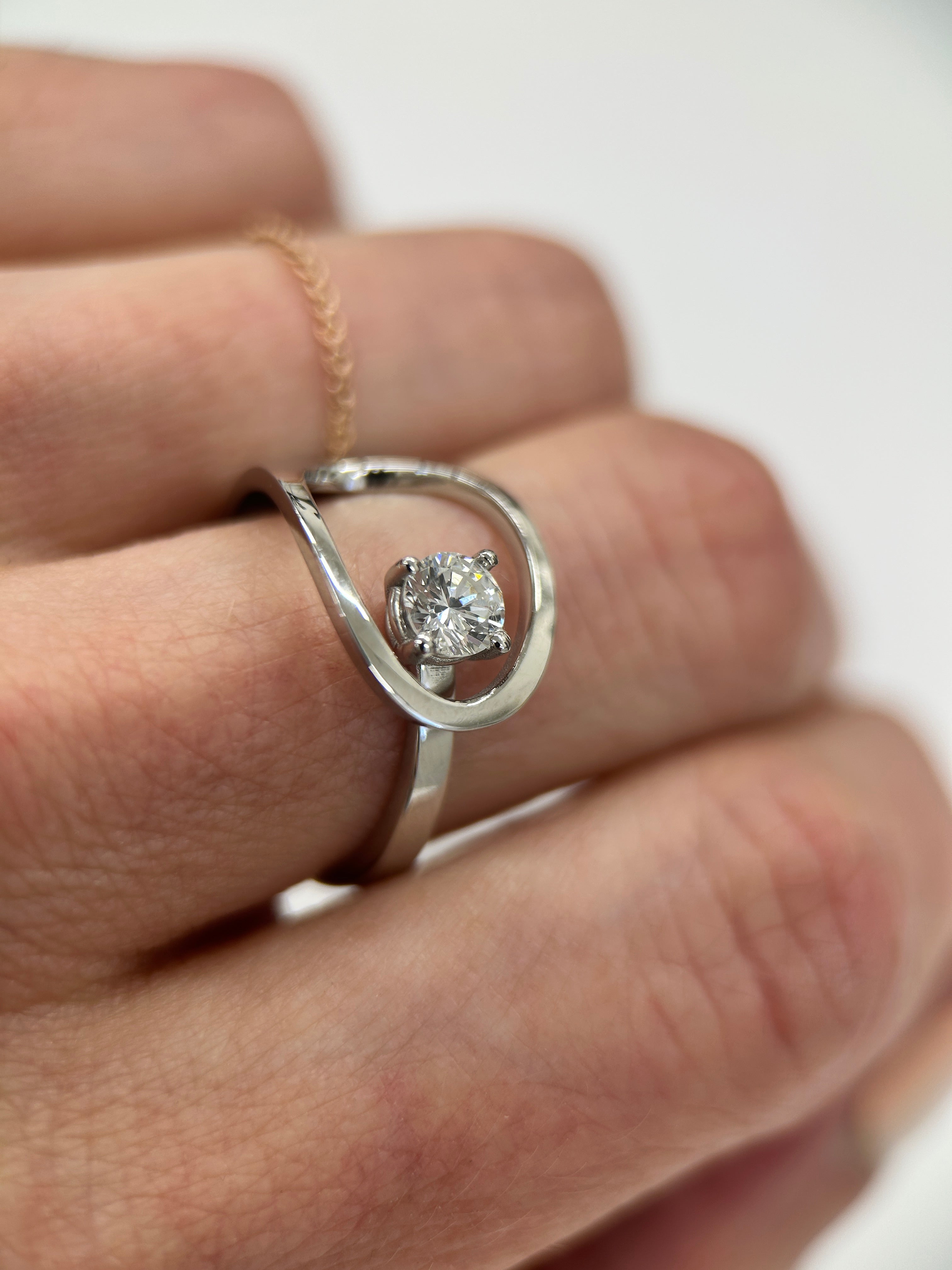 ring with a diamond on a person's finger against a white background