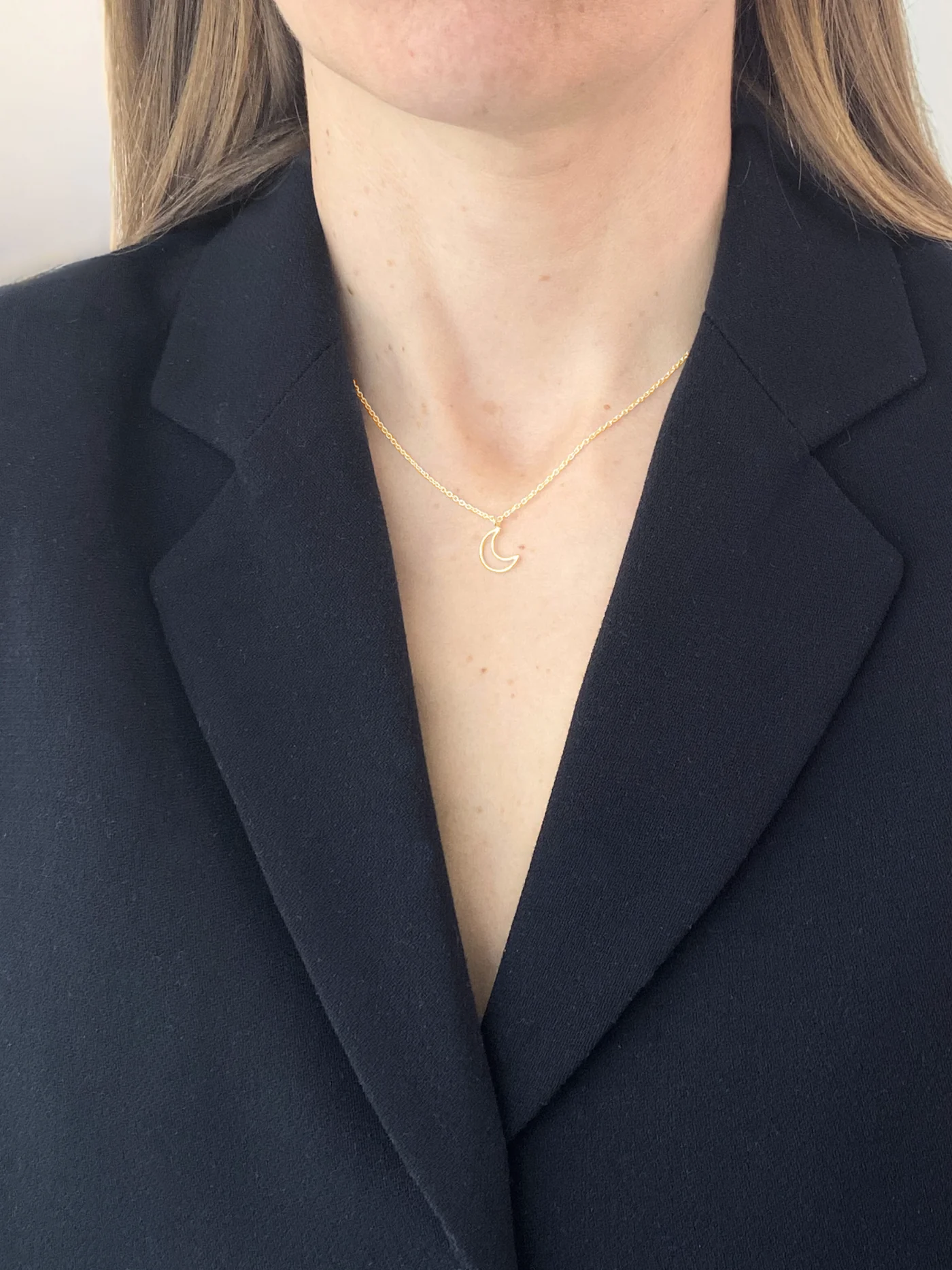 Person wearing a gold necklace with a small pendant against a dark blazer background