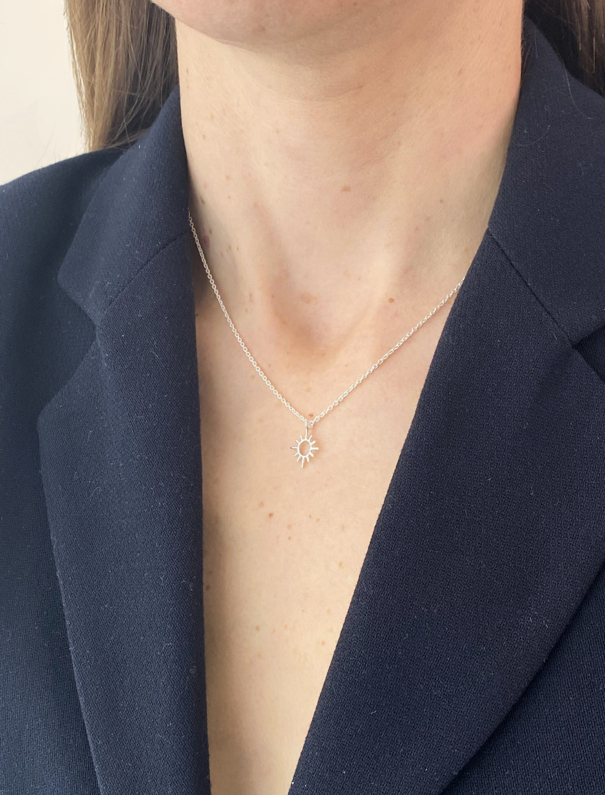 Person wearing a sun necklace with a navy blazer