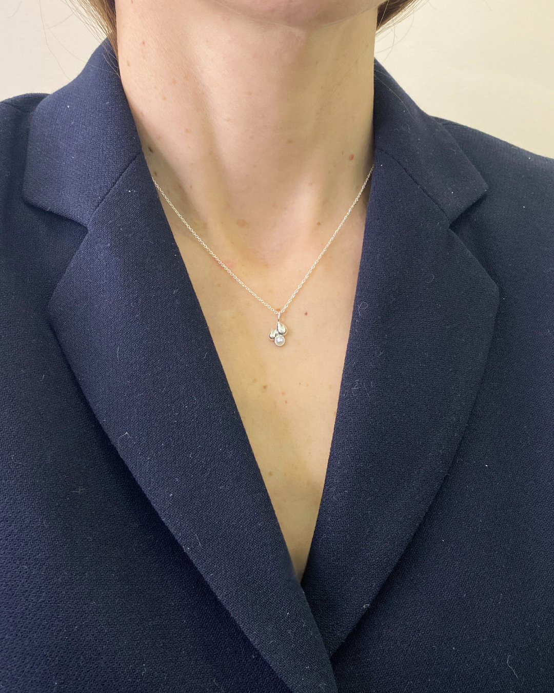Person wearing a navy blazer with a necklace featuring a small pendant.