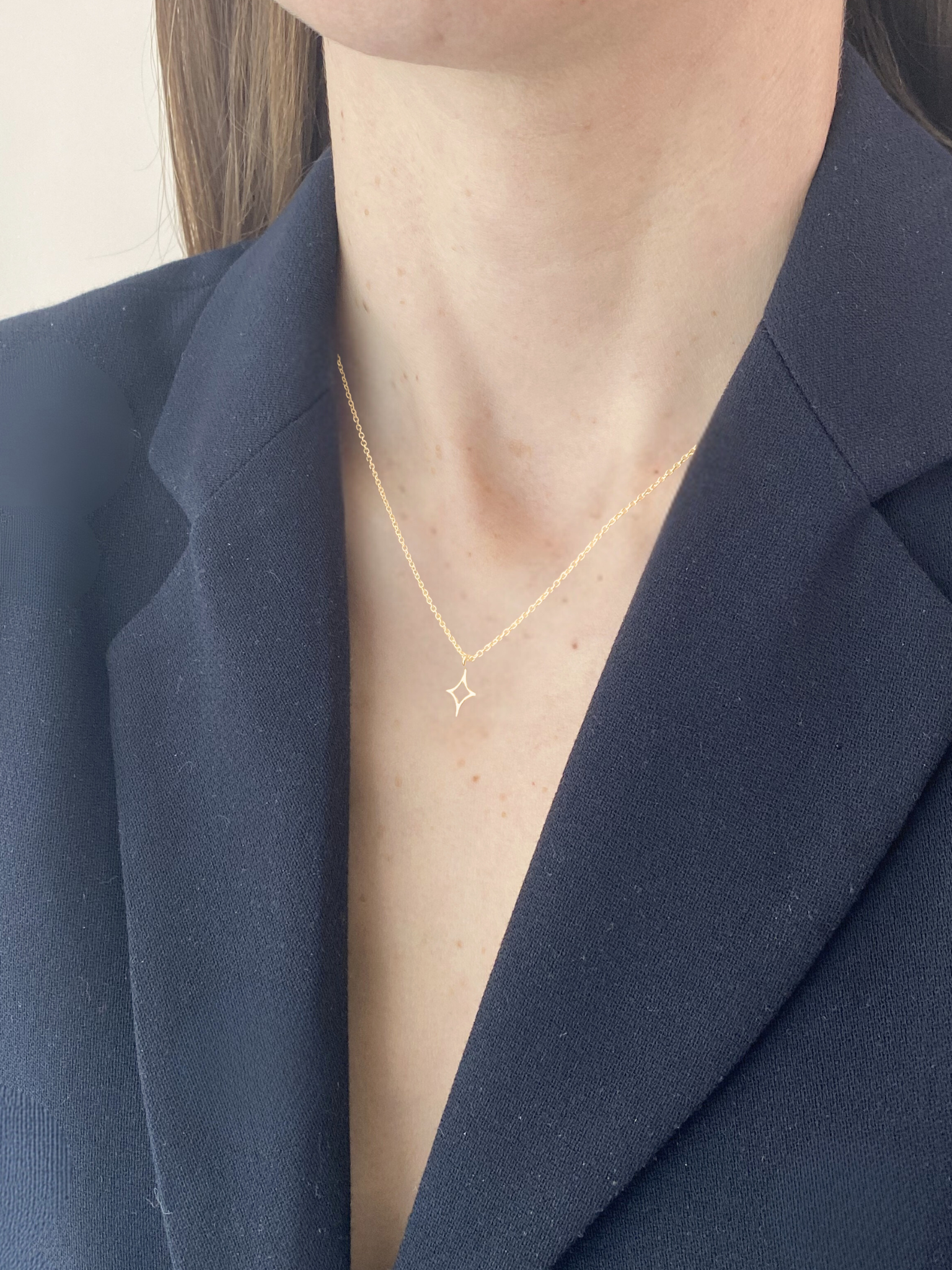 Person wearing a gold star necklace with a star pendant against a navy blazer.
