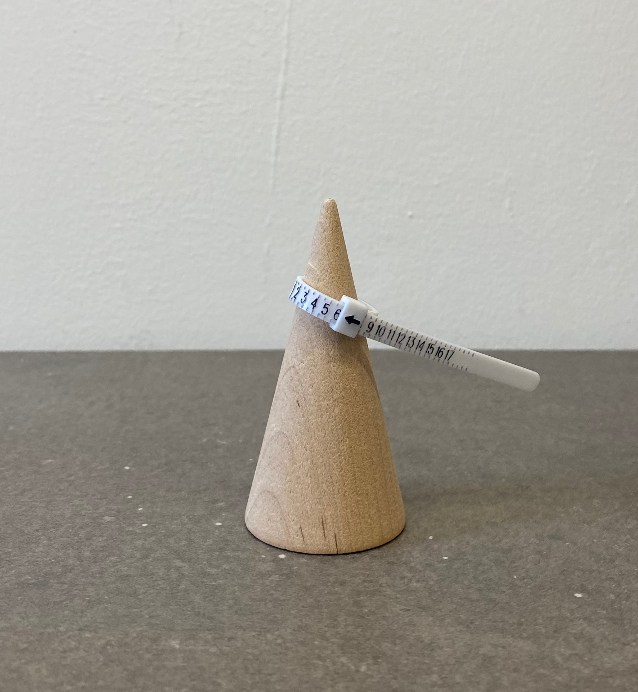 Small wooden cone with a ring sizer on a gray surface and white background